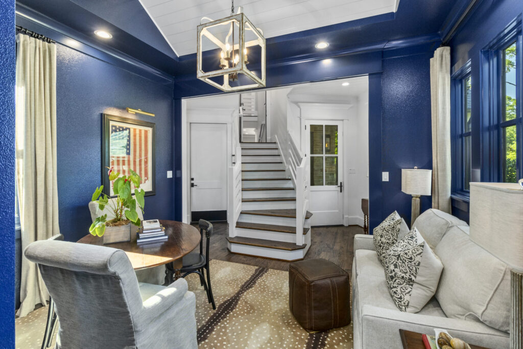 A small sitting room with blue walls, a sofa, chairs, a round table, and a staircase leading to the upper floor.