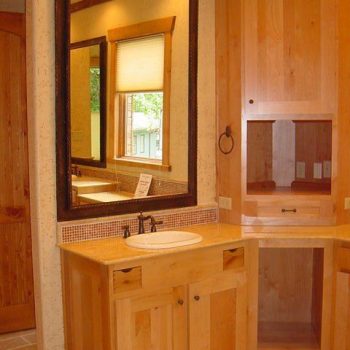 Wooden bathroom vanity with a large mirror, single sink, and surrounding wood cabinetry.
