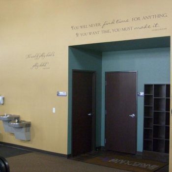 Two dark doors and open cubbies set in a gym wall; motivational quotes are written above the doorway.