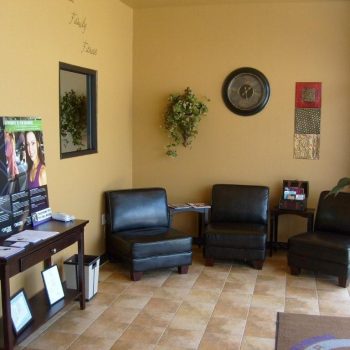 Small waiting room with four black chairs, wall decor, informational brochures, and a table on a tiled floor.