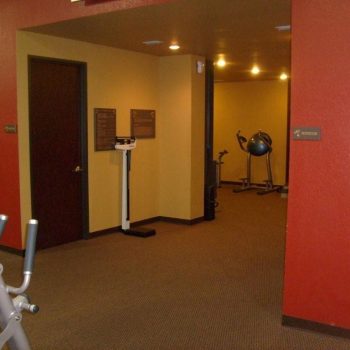 A small gym room with exercise equipment, a scale, and red and yellow walls with brown carpet flooring.