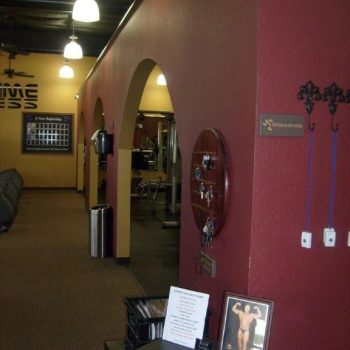 Interior of a gym with red and yellow walls, arched doorways, gym equipment, and a display table near the entrance.