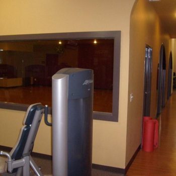 Exercise machine in a gym room near a hallway with a large window overlooking an empty studio space.