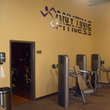Interior of a gym with exercise machines and an "Anytime Fitness" logo on a yellow wall.