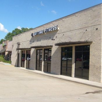 A beige brick strip mall with glass storefronts, including an Anytime Fitness gym, on a clear day.