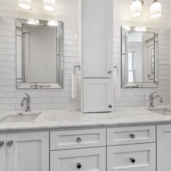 Double vanity bathroom with white cabinets, marble countertop, two mirrors, and modern light fixtures above each sink.