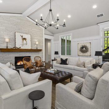 Modern living room with white sofas, stone fireplace, wall art, chandelier, and a black grand piano by large windows.