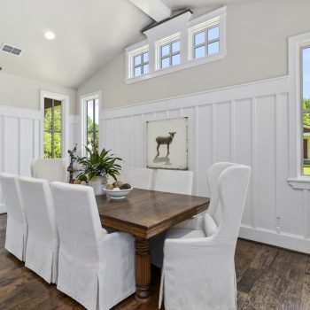 Dining room with a wooden table, six white slipcovered chairs, and a framed lamb picture on the wall.