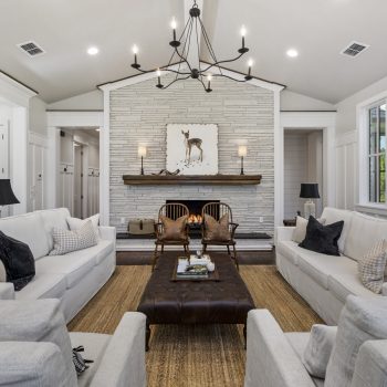 Modern living room with white sofas, a brown ottoman, a fireplace, and a deer art piece above the mantel.