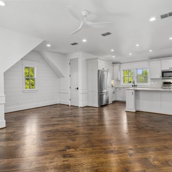Modern kitchen with stainless steel appliances and white cabinets, open to a living area with hardwood floors and white walls.