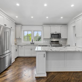 Modern kitchen with white cabinets, stainless steel appliances, marble countertops, and hardwood floors.