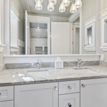 Modern bathroom with a marble countertop, double sinks, white cabinetry, and a large mirror reflecting the shower area.