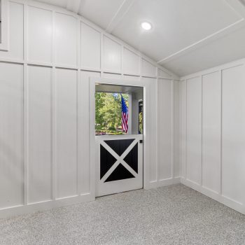 White paneled room with a Dutch door open to a view of trees, grass, and an American flag outside.
