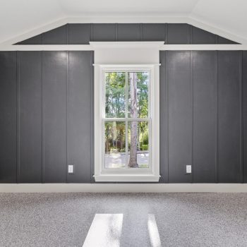 Empty room with dark gray paneled walls, a single window in the center, and light carpeted floor.