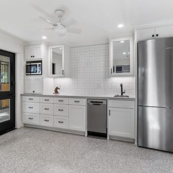 Modern kitchen with white cabinets, stainless steel appliances, black sink fixture, and a black door to the left.