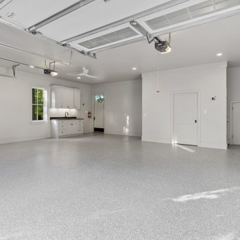 Spacious, clean garage with epoxy floor, white walls, built-in cabinets, sink, and open garage doors letting in light.