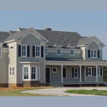 Two-story beige house with dark shutters, a large covered front porch, and a gabled roof, set on a grassy lot.