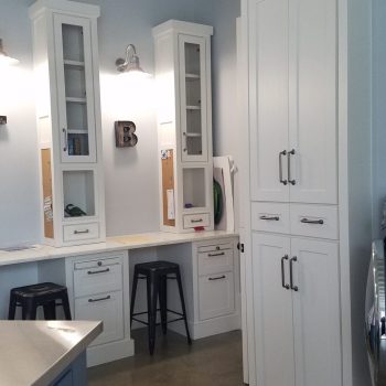 White cabinets and a workspace with stools and shelves in a modern kitchen with a concrete floor and blue accents.