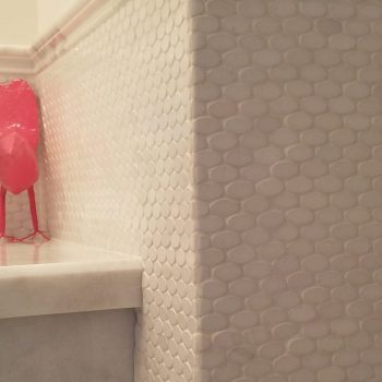 White textured tile wall with a marble countertop and a pink object partially visible on the left.