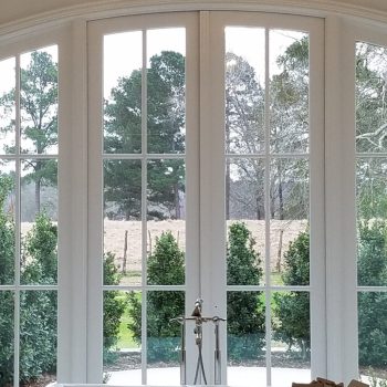 Freestanding bathtub with towels in front of large windows overlooking trees and greenery, under a hanging light fixture.