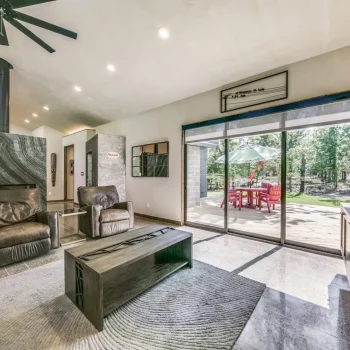 Modern living room with two leather chairs, a coffee table, large windows, and a view of a patio with red chairs outside.