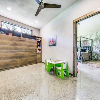 Modern room with a Murphy bed, bookshelves, kids’ play table, and an open doorway to a living area.