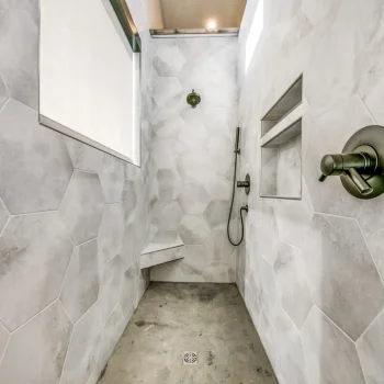 Modern walk-in shower with hexagonal light gray tiles, built-in niche, bench, and brushed metal fixtures.