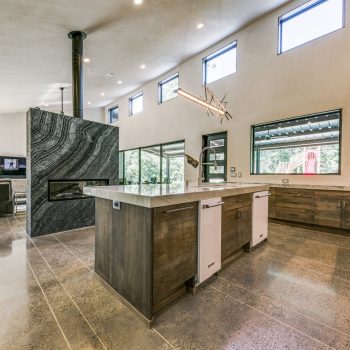 Modern kitchen with polished concrete floors, wood cabinetry, large island, and high windows letting in natural light.