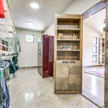 Walk-in closet with clothes on shelves, a hidden door bookshelf, and a visible safe in the adjacent room.
