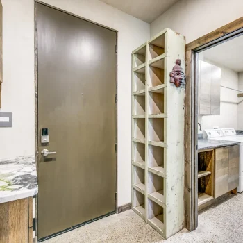 Laundry room with a washing machine, dryer, open shelving, countertop, and a closed brown door.