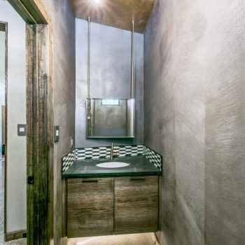 Modern bathroom with grey textured walls, underlit floating vanity, geometric backsplash, and a ceiling light fixture.