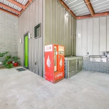 Outdoor kitchen area with a red vintage Coca-Cola vending machine, stainless steel grill, and gray cabinets.