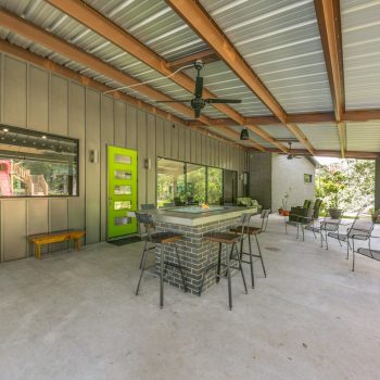 Covered patio with a modern fire pit, metal roof, ceiling fans, chairs, and a green door leading inside.