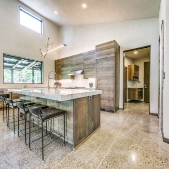 Modern kitchen with wood cabinets, island with barstools, polished concrete floor, and decorative African mask on the wall.