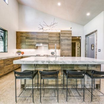 Modern kitchen with wood cabinets, marble island, four metal bar stools, and contemporary light fixture.