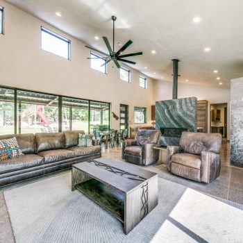 Modern living room with leather furniture, large windows, ceiling fan, and a view of a patio and backyard playground.