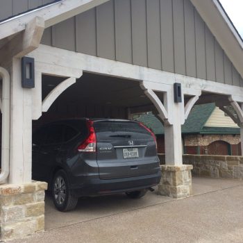 A black Honda CR-V is parked in a covered carport attached to a house with stone and wood pillars.