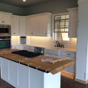 Modern kitchen with white cabinets, a farmhouse sink, stainless appliances, and an island covered in cardboard.