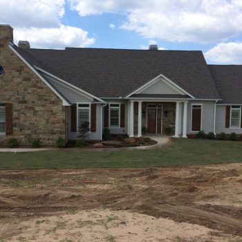Single-story house with stone and siding exterior, front porch, and a lawn under construction on a partly cloudy day.