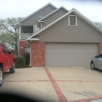 Two cars are parked in the driveway of a two-story brick and siding suburban house with a double garage.