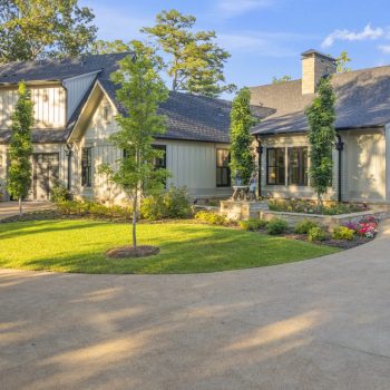 Modern two-story house with gray siding, large windows, landscaped yard, and a curved driveway on a sunny day.