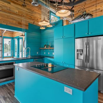 Modern kitchen with bright turquoise cabinets, stainless steel appliances, and large windows overlooking a body of water.