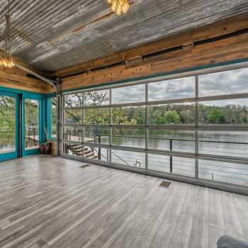 Room with wood and metal accents, large glass garage door open to a lake view, and light wood flooring.