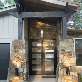 Modern house entrance with stone pillars, glass double doors, and a covered porch with outdoor wall lights.
