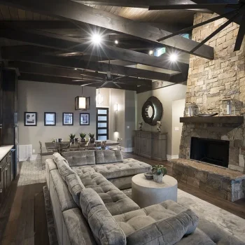 Modern living room with stone fireplace, exposed wood beams, gray sectional sofa, and neutral decor.