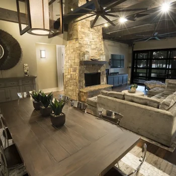 Modern living and dining area with wooden furniture, stone fireplace, large sectional sofa, and view of lake through glass doors.
