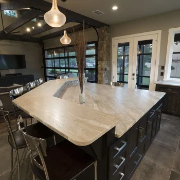 Modern kitchen with a large, angled island, metal chairs, pendant lights, and lake view through glass doors and window.