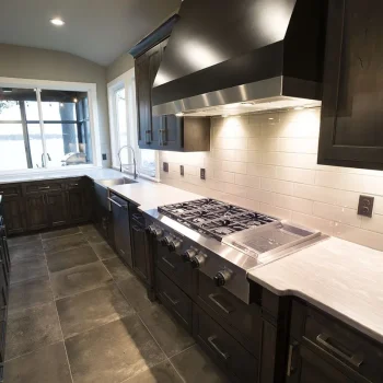 Modern kitchen with dark cabinets, stainless steel appliances, gas stove, tile flooring, and large windows.