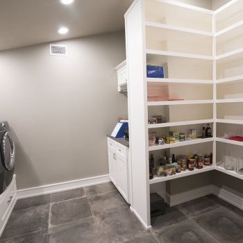Modern laundry room with washer, dryer, white cabinets, and an adjacent pantry with shelves holding various food items.