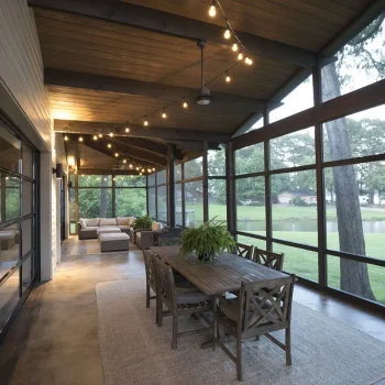 Screened-in porch with string lights, wooden dining table, and outdoor seating, overlooking a grassy yard and trees.